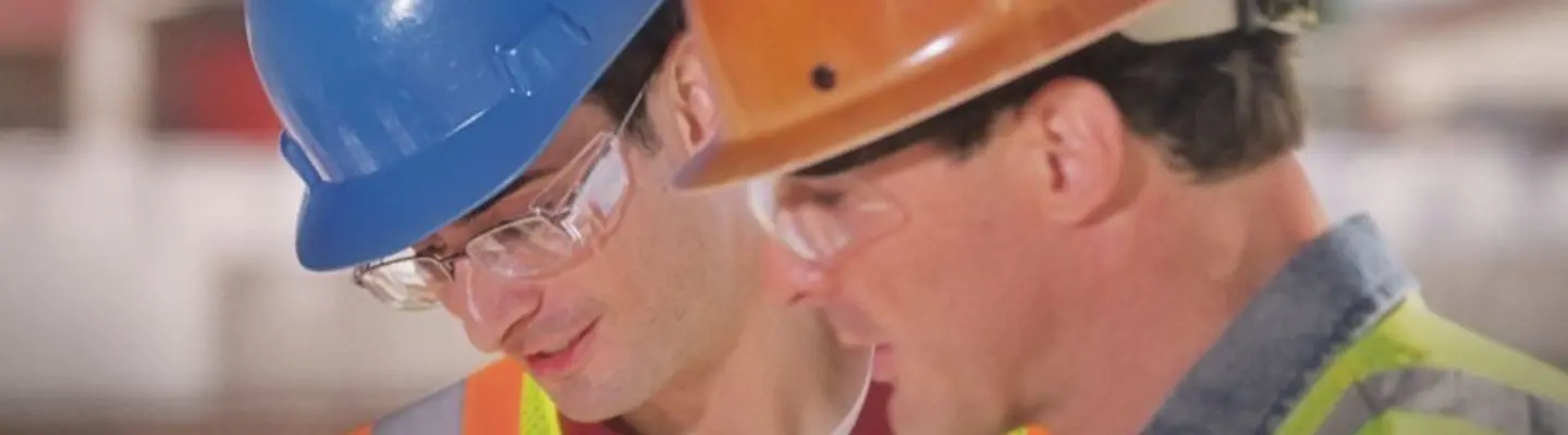 Two men on a construction site wearing hard hats, safety vests and safety glasses.