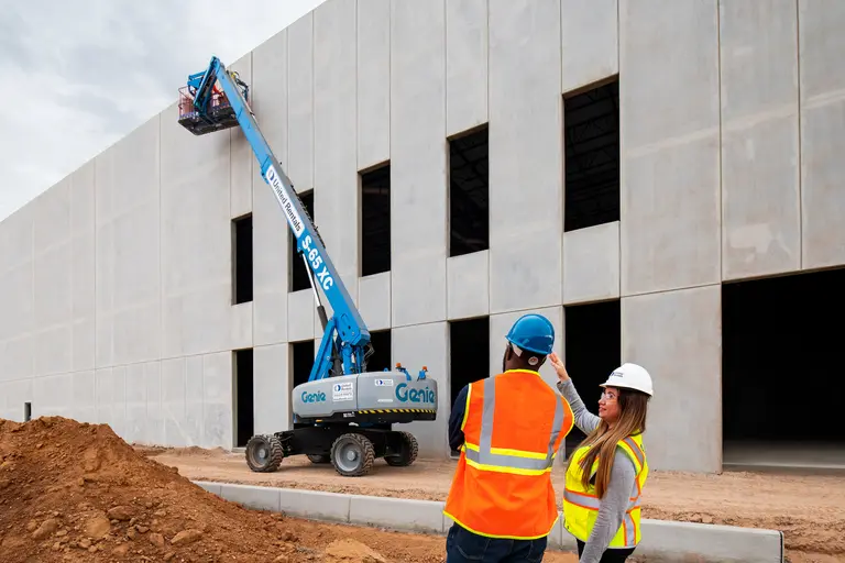 workers in safety vests looking at blue boom lift next to building