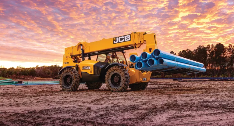 Telehandler moving pipes at sunset