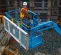 Top view of a blue boom lift platform with safety railing, operator wearing safety gear, elevated on a construction site.