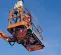 Bottom up angled view of two workers in safety gear in a scissor lift basket, elevated on a clear blue sky background.