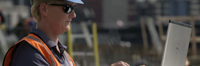 Worker at a jobsite wearing PPE and using a laptop computer