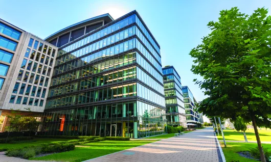 stock image of the outside of a glass office building near trees under a blue sky