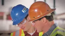3 men looking at computer screen, one man pointing. All men are wearing hats and safety glasses