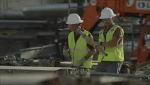 Two men on a construction site wearing hard hats, safety vests and safety glasses.