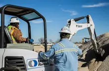 woman in mini excavator next to man near dirt pile